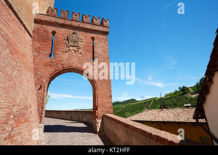 Barolo medieval castle entrance arch in red bricks and emblem with empty street in a sunny summer day, blue sky Stock Photo