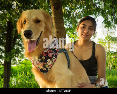 Asian woman playing with her golden retriever dog in a park outdoors ...