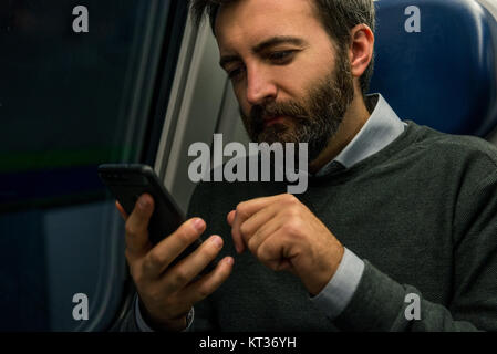 Youn adul man commuter businessman seated on train look at smartphone during travel in the evening. Stock Photo