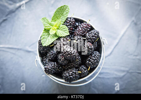 Fresh organic black mulberry in a small basket with mint leaves. Stock Photo