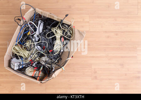 Old battered cardboard box with electrical cords and connectors for electronic devices on a wooden background with copy space viewed from above Stock Photo