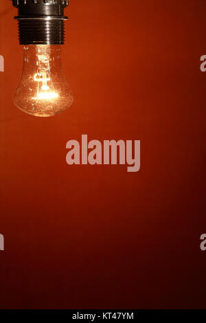 Closeup of glowing light bulb on nice red wall background Stock Photo