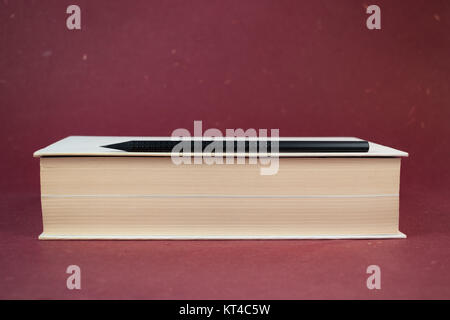 White hardcover book with black wooden pencil on red background, surface. Stock Photo