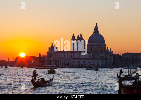 Colourful orange sunset over the Venice lagoon and Basilica di Santa Maria della Salute with  gondolas with tourists in ta romantic scene Stock Photo