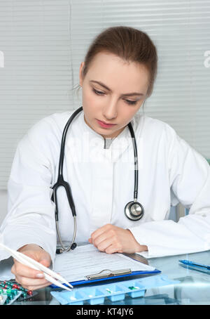 Physician or nurse in white coat selects pills for a patient checking his records Stock Photo