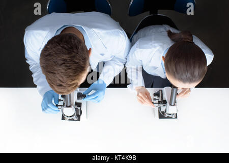 top view of scientists in uniforms looking through microscopes in laboratory Stock Photo