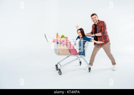 Happy young man pushing shopping cart with excited woman and grocery bag on white Stock Photo