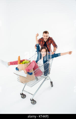 Smiling young man pushing shopping cart with excited young woman and grocery bag Stock Photo
