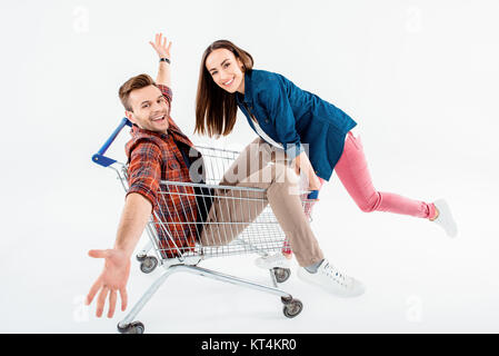Smiling young woman pushing shopping cart with excited young man on white Stock Photo