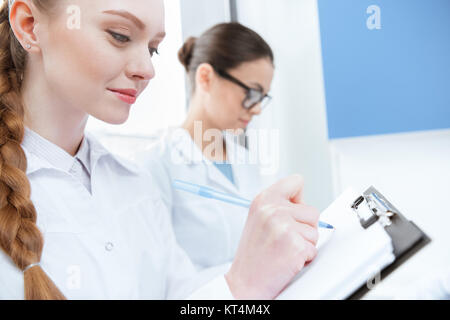 Young women scientists in white coats taking notes in laboratory Stock Photo