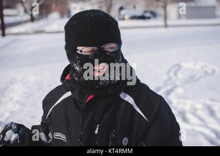 A young boy wearing a winter ski mask plays in the snow during the day. Stock Photo