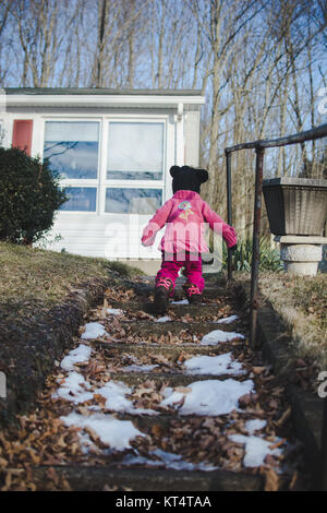 A child climbs up a flight of stone stairs wearing a sweater during the winter Stock Photo