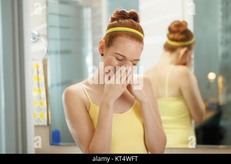 Redhead girl applying beauty cream in home bathroom at morning. Young woman taking care of her skin, looking and smiling intimately. Female beauty, sk Stock Photo