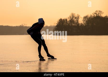 Ice speed skating silhouette in orange light of setting sun on frozen lake in the Netherlands Stock Photo