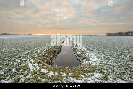 Frozen grassland with straight river canal in center dissapearing on horizon Stock Photo