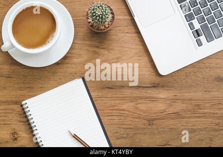 Wooden desk table with notebook, computer laptop, pencil, cactus and cup of coffee. Top view with copy space Stock Photo