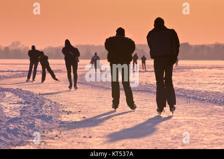 Ice Skaters on frozen lake seen on their back under orange sunset Stock Photo