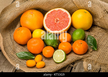 Close-up view of various whole and sliced fresh citrus fruits on sackcloth