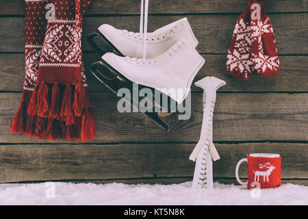 red scarf with gloves and white skates hanging on striped wall  Stock Photo
