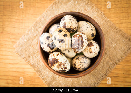 Quail eggs in a bowl on sacking on a wooden surface, top view, empty place for text, recipe Stock Photo