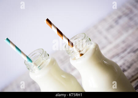 Two bottles of milk with striped straws standing on old table. Stock Photo