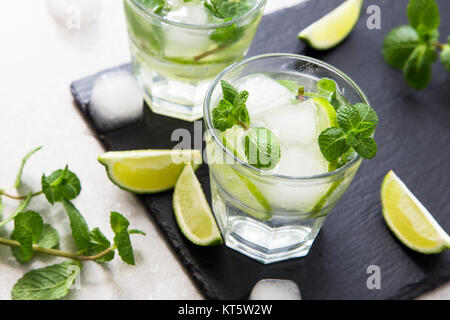 Cold refreshing summer lemonade mojito in a glass on a slate board and stone background.