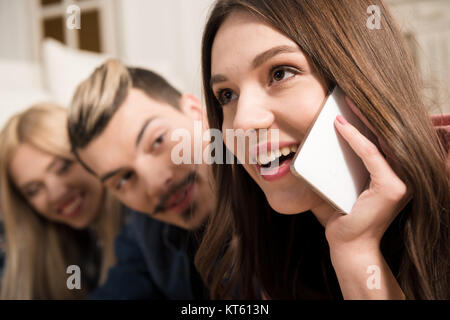 Smiling young friends looking at beautiful happy woman talking on smartphone Stock Photo