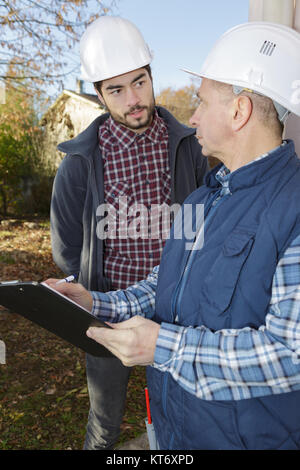 two builders in hardhats with clipboard outdoors Stock Photo