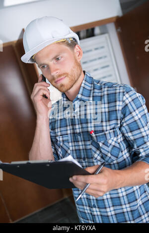 busy construction engineer talking on phone and holding clipboard Stock Photo