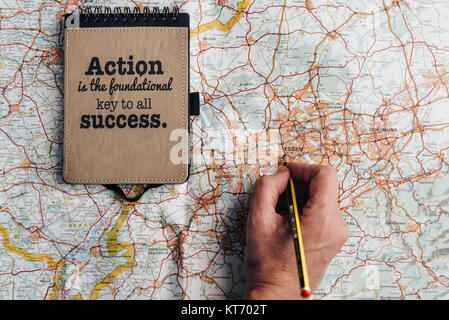 Lay flat of woman hand with pencil on map, notebook with motivational quote and phone. Conceptual, planning Stock Photo