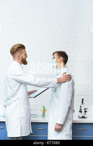side view of scientists in white coats discussing experiment results in lab Stock Photo