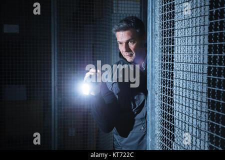 Security Guard Using Flashlight In The Warehouse Stock Photo