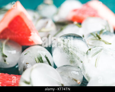 Close up view of detox rosemary ice cubes and fresh rosemary slice over green cement background. Stock Photo