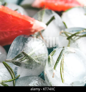 Close up view of detox rosemary ice cubes and fresh rosemary slice over green cement background. Stock Photo