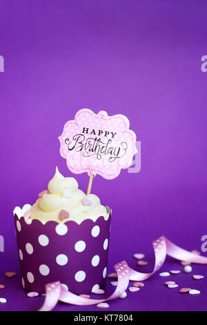 Cupcake with small decorative hearts and happy birthday sign, against violet background Stock Photo