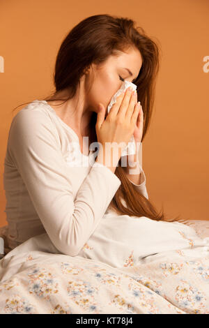 illness flu - Young Woman Lying On Bed Infected With Allergy Blowing Her Nose Stock Photo