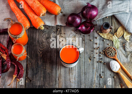 Carrot juice in glass jars and iron mug on a gray wooden surface Stock Photo