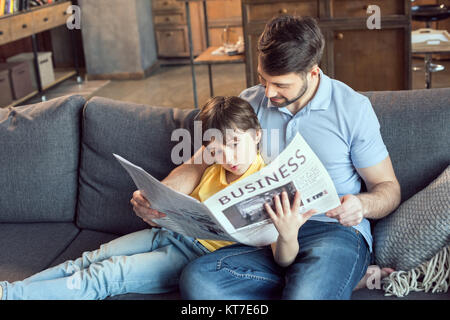 focused son reading newspaper to father at home Stock Photo