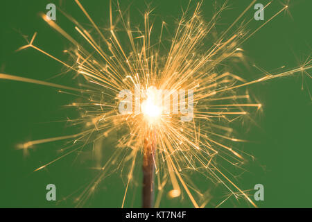 Burning yellow sparkler close up on green background. Stock Photo