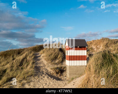Small red and white striped hut standing on the beach dunes with sea views Stock Photo
