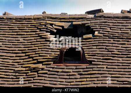 Old damaged tiled roof with a hole on the roof and broken tiles Stock Photo