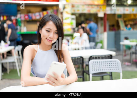 Woman sending sms on cellphone at outdoor restaurant Stock Photo