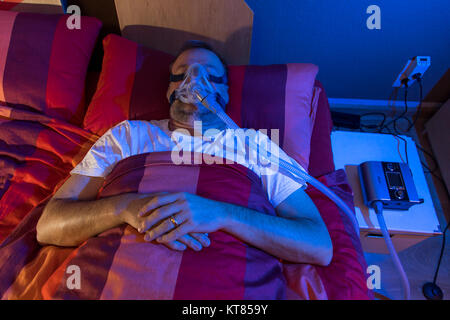 A man with sleep apnea syndrome, wears a CPAP mask while sleeping, breathing mask that presses air into the airways by overpressure, preventing airway Stock Photo