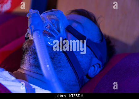 A man with sleep apnea syndrome, wears a CPAP mask while sleeping, breathing mask that presses air into the airways by overpressure, preventing airway Stock Photo