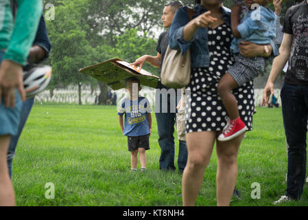 David Hernandez holds a cardboard box over his son, David Hernandez Jr., as they wait in line to pick up flowers from Memorial Flower Foundation in Arlington National Cemetery, Arlington, Va., May 28, 2017.  Volunteers lay roses at headstones every year during Memorial Day Weekend.  (U.S. Army photo by Elizabeth Fraser / Arlington National Cemetery / released) Stock Photo