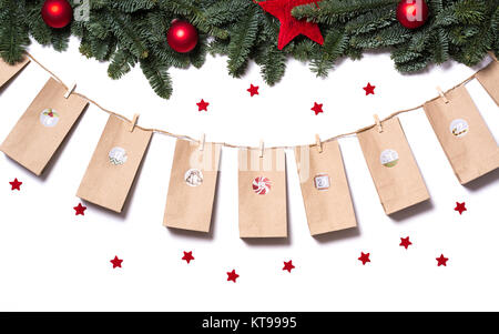 Handmade tinkered advent calendar with paper bags and stickers hanging from fir branches and red stars on a white background Stock Photo