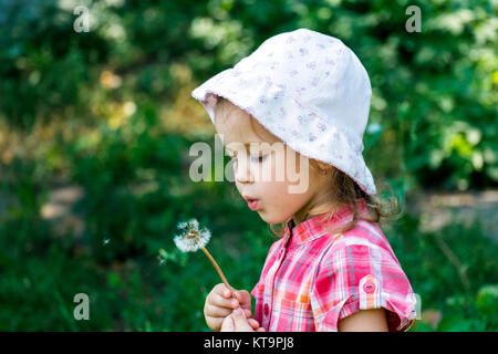 Little girl in a hat blowing a dandelion Stock Photo