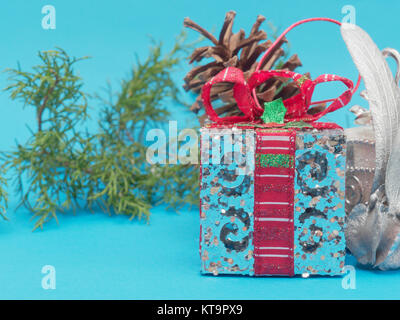 White shiny silver gift box with red ribbon and bow with white square and round shape gift box and pine cone and  branch over bright blue background i Stock Photo