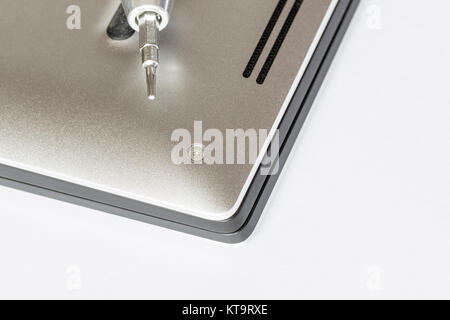 Top view of a hand with a screwdriver over disassembled notebook and screws against white background. Electronics professional service concept. Stock Photo