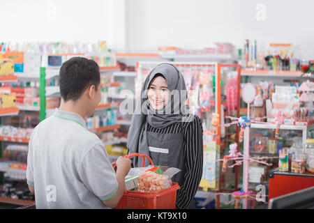 young asian muslim female shopkeeper or cashier welcoming customer at supermarket Stock Photo